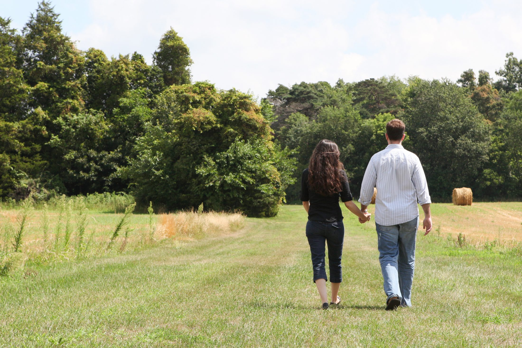 DC widow blog writer Marjorie Brimley walks away from camera in field holding hands with husband Shawn