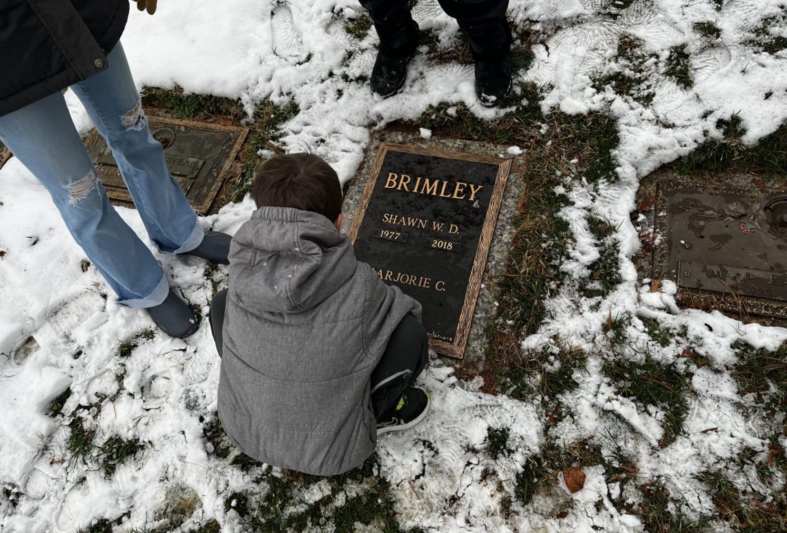 Tommy Brimley, son of DC widow writer Marjorie Brimley Hale, kneels by his father's grave